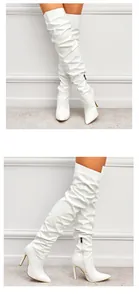 Gros plan de bottes cuissardes en cuir verni blanc avec talons hauts aiguilles.