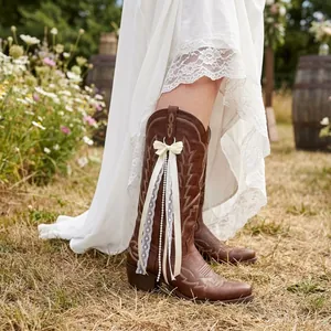 Detail view of a white ribbon bow accessory with lace and pearls on a brown cowboy boot.