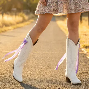 Detailed view of elegant purple ribbon bow charms on white Western cowboy boots outdoors