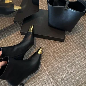 Detail of black leather ankle boots featuring a prominent gold metal pointed toe cap.