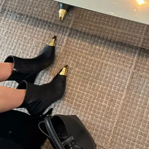 Detail of black stiletto ankle boots with gold metal toe cap and side zipper