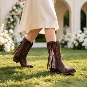 Close-up of brown western boots decorated with ribbon and lace pearl charms on grass