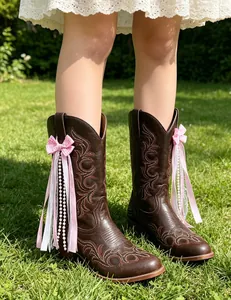 Detail of pink bow ribbon and pearl accessories on brown cowboy boots outdoor