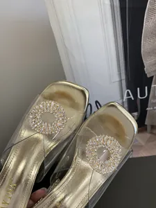 Detailed view of gold high heel slippers with clear PVC strap and rhinestone buckle