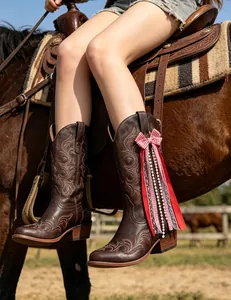Detailed macro view of a red plaid bow ribbon charm attached to a brown western boot.