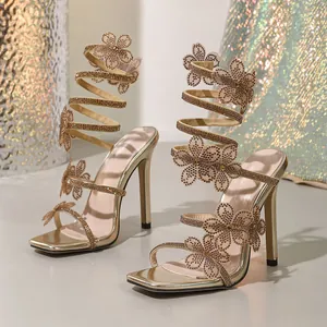 Detailed view of gold rhinestone flower sandals with stiletto heels and spiral wraps.