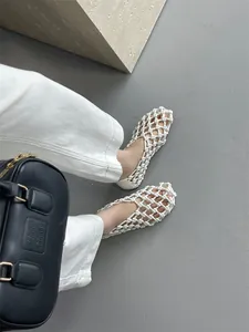 Close-up of white woven hollow-out sandals worn by a model on a stylish concrete surface