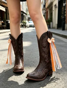 Close-up of decorative orange ribbons and lace pearls on vintage brown western boots