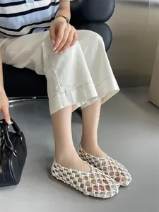 Close-up view of elegant white hollow woven flat sandals worn by a model in style