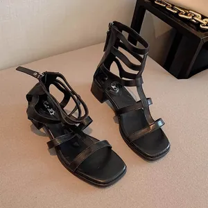 Détail de sandales romaines noires à lanières avec talon bloc et fermeture éclair.