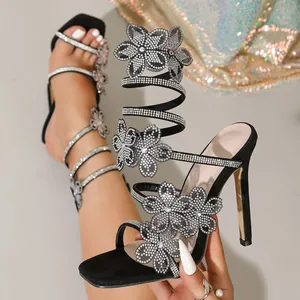 Close-up of elegant black stiletto sandals featuring rhinestone flowers and a snake spiral wrap.