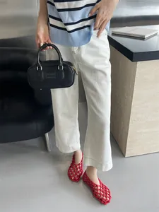 Red hollow woven flat shoes styled with white trousers and a black handbag for a chic look.