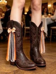 Detailed view of orange ribbon bows with pearls and lace hanging on brown cowboy boots
