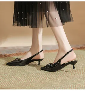 Elegant black patent leather pointed toe kitten heel slingbacks worn with a skirt.