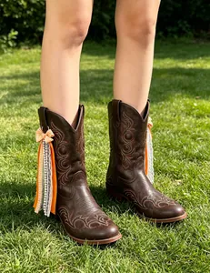 Detail shot of orange checkered ribbon and pearl charms attached to brown western boots