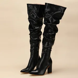 Fashionable black pleated over-the-knee boots with high chunky heels in studio lighting.