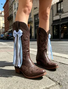 Close-up detail of light blue ribbon and pearl bow charms on brown Western boots