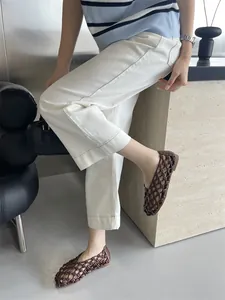 French style hollow woven flat sandals in brown, styled with white trousers.