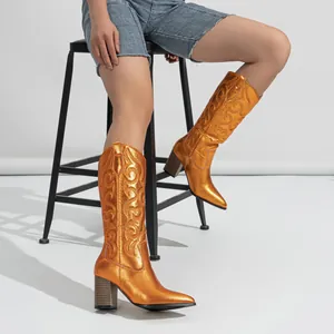 Close-up detail of shiny metallic orange embroidered cowboy boots featuring block heels