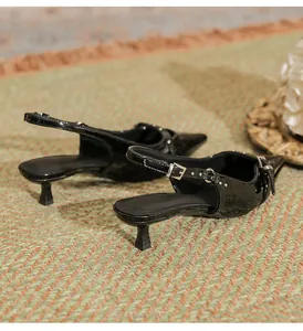 Detailed macro view of black patent leather kitten heel slingback sandals on a textured mat