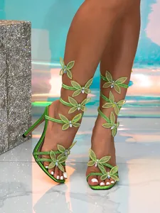 Detailed close-up of vibrant green butterfly rhinestone wrap-around stiletto heels on model