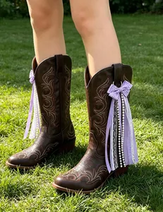 Detailed view of handmade purple ribbon and pearl charms attached to brown cowboy boots.