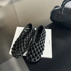 Detail view of black woven hollow-out flat sandals presented in a luxury fashion scene