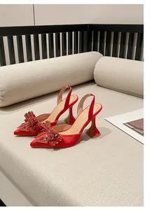 Elegante rote Satin-Pumps mit Strassschleife und Weinglas-Absatz auf beigem Sofa