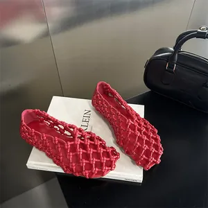 Macro view of stylish red hollow woven breathable women's flat shoes on a white prop book.