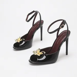 Elegant black patent leather peep-toe heels with gold flower detail and ankle strap