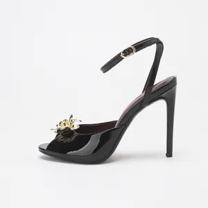 Elegant black patent leather peep-toe stiletto sandals with gold metal flower decoration.