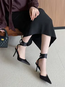 Detalle de tacones de aguja negros de punta con elegantes cintas de seda al tobillo.
