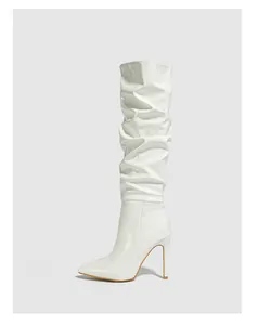 Macro detail of white patent leather slouch boots featuring stiletto heel and pointed toe.
