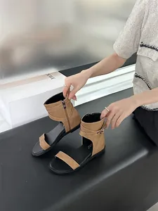 Detailed view of brown flat Roman sandals featuring ankle strap buckles and soft black soles