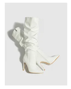 Detail view of white patent leather slouchy knee-high boots featuring sharp stiletto heels