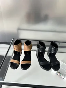 Two pairs of flat Roman sandals in tan and black displayed on a modern glass table.
