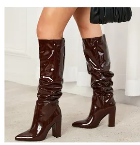 Macro view of brown patent leather slouchy boots featuring pointed toes and chunky high heels