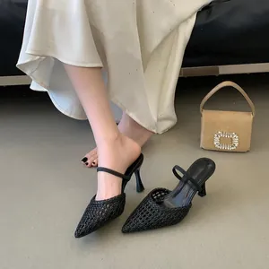 Detailed close-up of black pointed-toe woven hollow-out high-heel mules worn by a model.