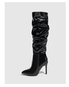 Detail of black patent leather slouchy knee-high boots with pointed toe and stiletto heel