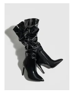 Close-up detail of glossy black patent leather slouchy knee-high boots with high stiletto heels