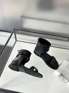 Close-up detail view of black flat Roman sandals featuring ankle buckles and side zipper
