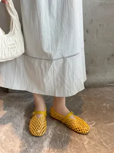 Detail view of yellow hand-woven hollow-out Mary Jane flats on feet with a white skirt