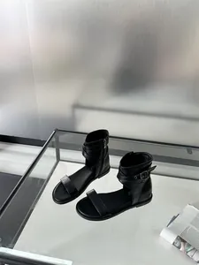 Close-up view of elegant black flat Roman sandals with buckle straps on a glass table