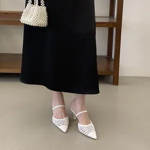 Detailed view of white woven pointed-toe kitten heel sandals paired with a black skirt