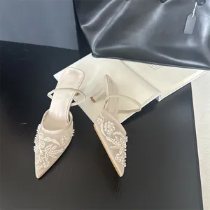 Close-up of elegant beige pointed-toe mules with white floral embroidery and pearls