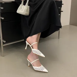 Detailed view of white pointed-toe woven hollow high-heeled mules worn with black dress.