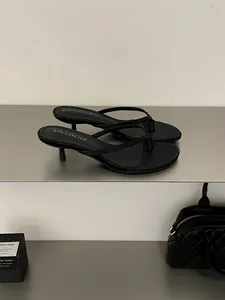 Eleganti infradito nere con tacco a spillo basso esposti su una mensola metallica minimalista.