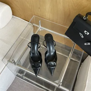 Close-up of black pointed-toe high heels with square buckle detail on glass table