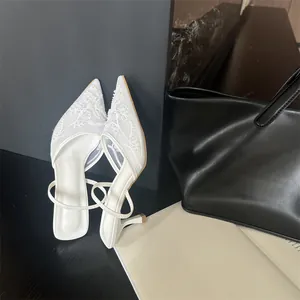 Close-up detail of elegant white mesh pointed-toe heels with floral embroidery.