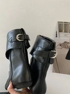 Detailed macro view showing the silver buckle and black leather texture of Chelsea boots